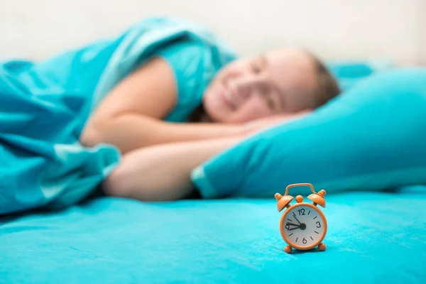 Menina adolescente deitada na cama e segurando um despertador laranja — Fotografia de Stock