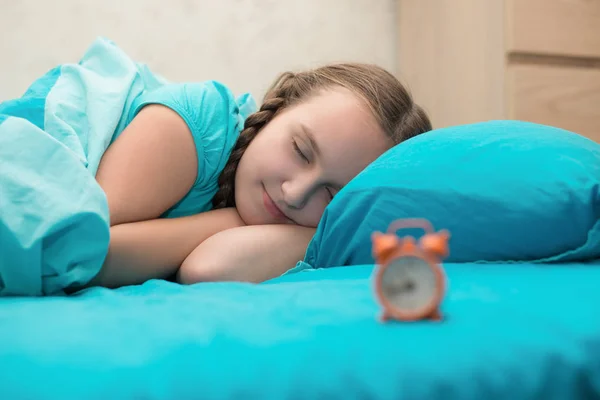 十几岁的女孩躺在床上和抱着橙色的闹钟 — 图库照片