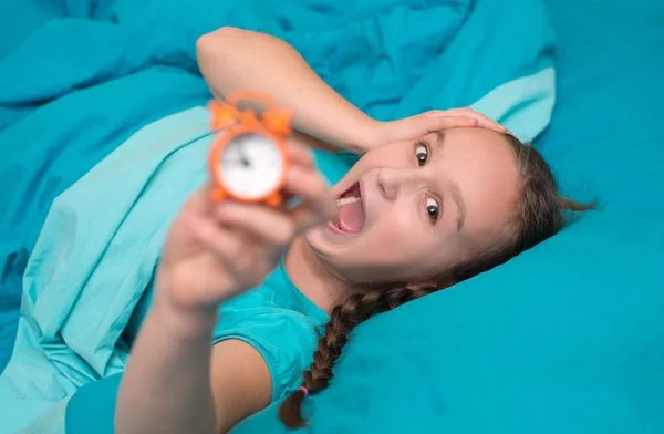 Девочка-подросток лежит в постели с оранжевым будильником — стоковое фото