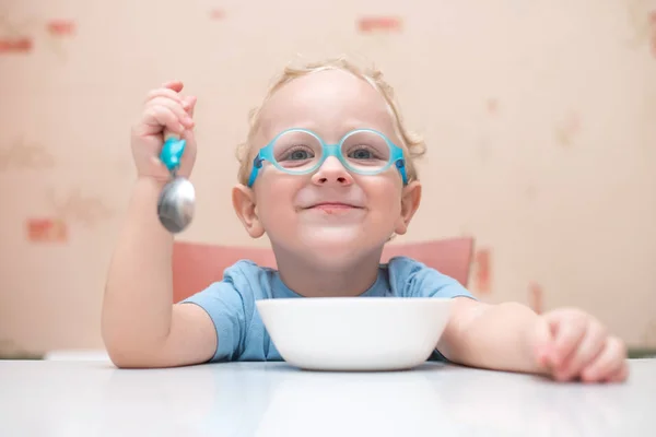 Ребенок в очках сидит за столом и держит ложку в руках — стоковое фото