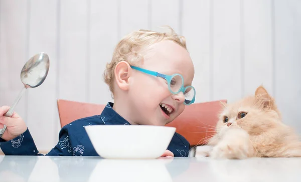 kedi ile masada oturan gözlüklü çocuk