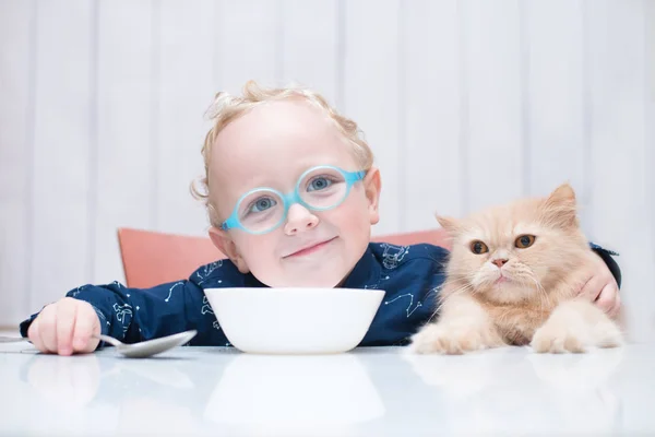 kedi ile masada oturan gözlüklü çocuk