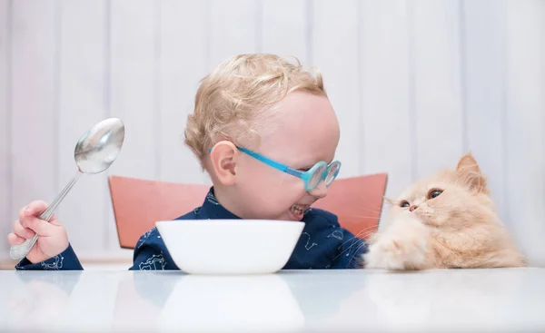 Ребенок в очках сидит за столом с котом — стоковое фото
