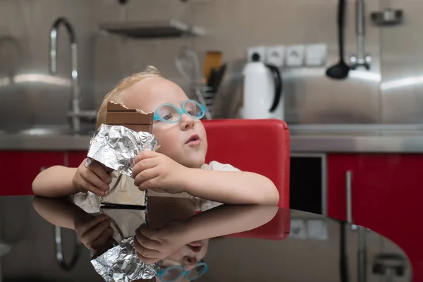 Ребенок в очках ест шоколад сидя за столом — стоковое фото