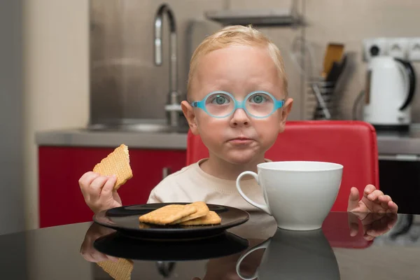 Ребенок в очках ест шоколад сидя за столом — стоковое фото