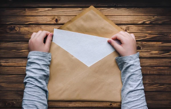 large brown envelope holds the child\'s hands. Open envelope on a wooden background. A blank sheet of paper in an envelope.