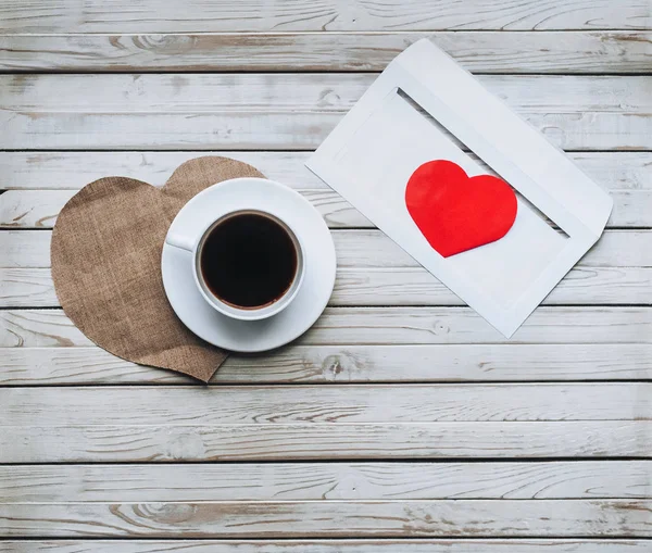 Cup of coffee and an envelope with a letter of love. The concept of St. Valentine\'s Day. Envelope with heart inside. Envelope on a wooden background.