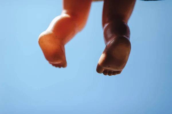 Feet of a plastic puppet doll on a sky background. Children games. The concept of loneliness