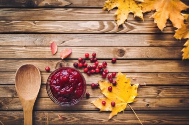 Kızılcık Reçeli, taze meyveler, tahta kaşık ve ahşap arka plan üzerinde sonbahar yaprakları. Sonbahar vitaminler