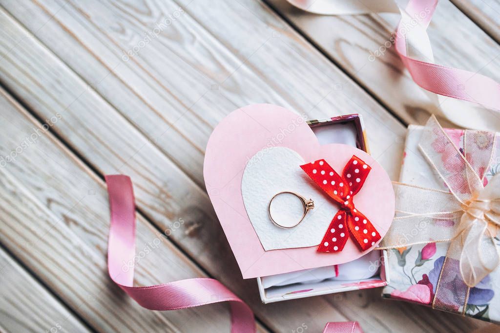 Marriage proposal concept. Wedding ring in gift box on wooden background. Valentine's Day. Festive decor.