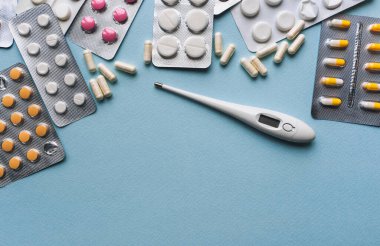 Kabarcıklı sarı, beyaz, pembe tabletler ve mavi arka plan manzaralı termometre. Tıbbi eczane konsepti. Geleneksel tıp. Boşluğu kopyala.