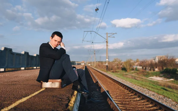 Depressed young sad businessman sitting on suitcase head in hands on the railway platform alone, Cry, drama concept.