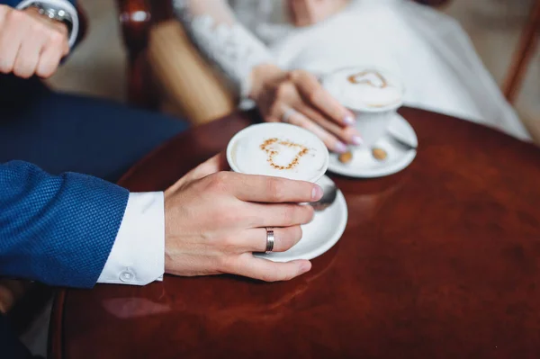 新婚者のカップルは 一杯のコーヒーのための美しいカフェに座っています カプチーノの泡と白いカップは 心のシンボル — ストック写真