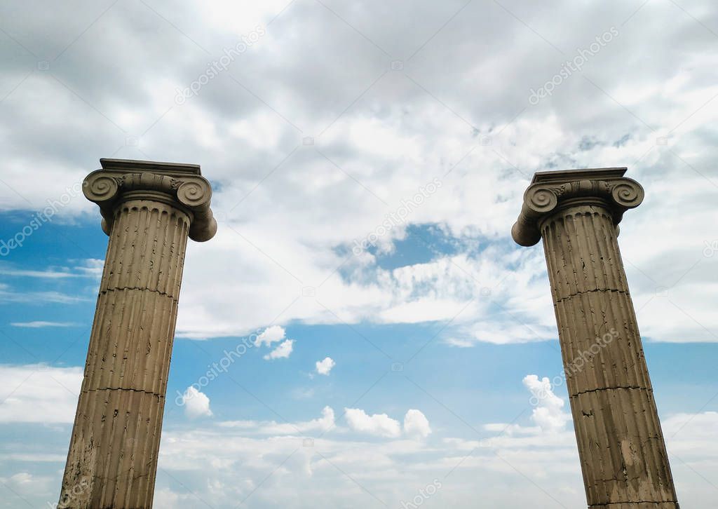 Two antique Ionic marble columns against a cloudy sky. The concept of antique art, ruins and historical architecture.