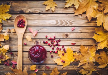 Sonbahar vitaminleri. Ahşap bir arka planda kızılcık ve sonbahar yaprakları. Gribi önleme, beriberi. Kızılcık reçeli.