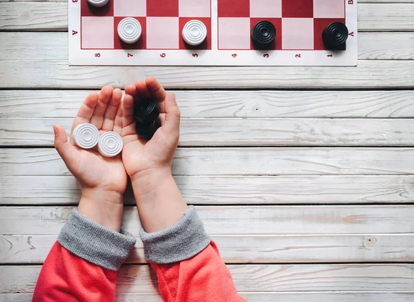 The child plays checkers. White and black checkers in children\'s hands. Children\'s school of board games.