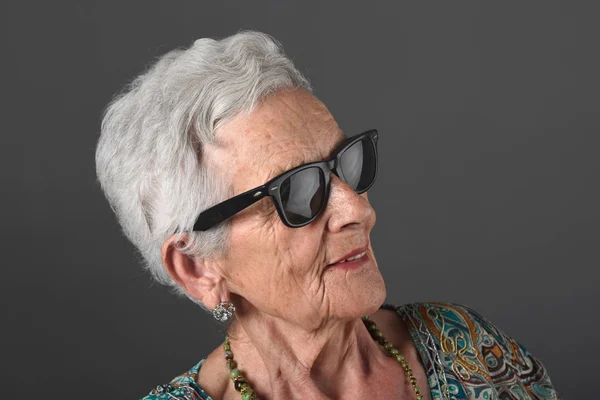 Retrato de uma mulher idosa com óculos de fundo cinza — Fotografia de Stock