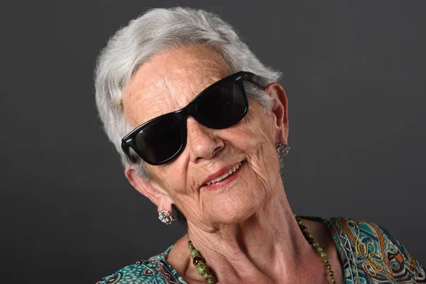 Retrato de uma mulher idosa com óculos de fundo cinza — Fotografia de Stock