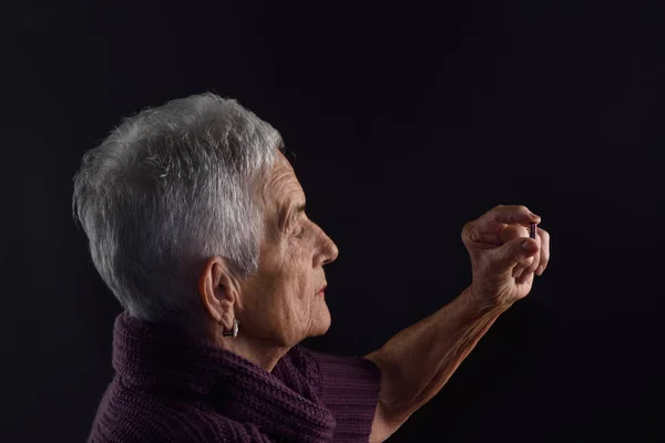 Senior vrouw op zoek een pil met grijze achtergrond — Stockfoto