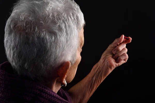 Senior vrouw op zoek naar een pil van rode kleur — Stockfoto