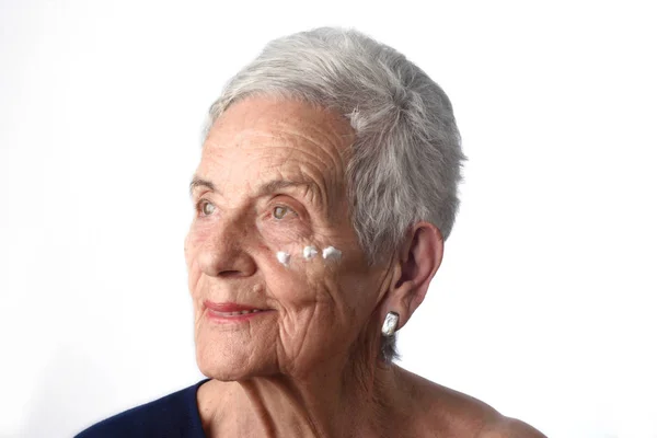 Senior vrouw toepassing huid crème of crème op haar gezicht — Stockfoto