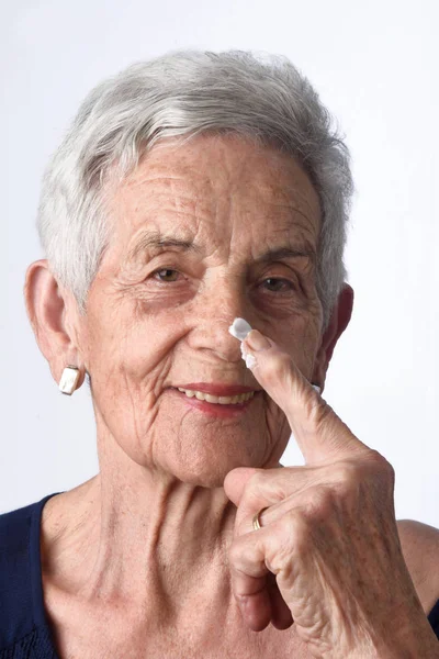 Senior woman applying skin cream or moisturiser to her face — Stock Photo, Image