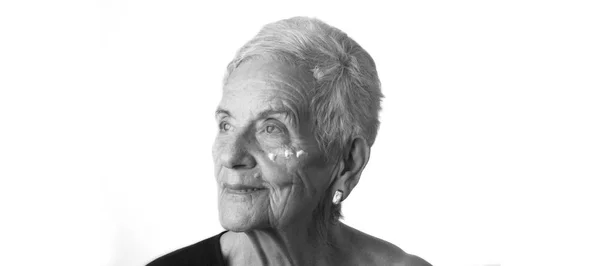 Старшая женщина наносит крем для кожи или увлажняющий крем на лицо — стоковое фото