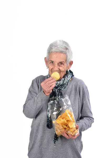 Senior woman eating chips, isolated on white — Stock Photo, Image