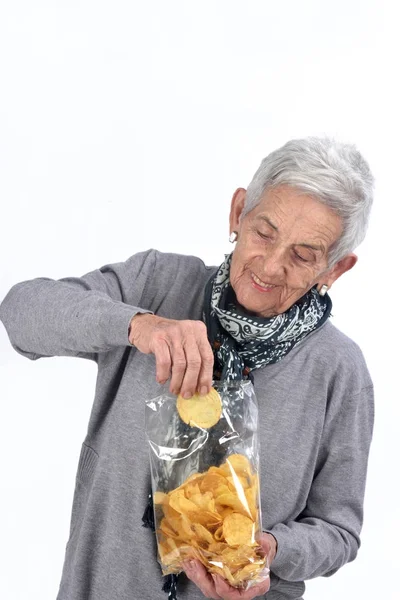 Senior kvinna äter chips på vit — Stockfoto