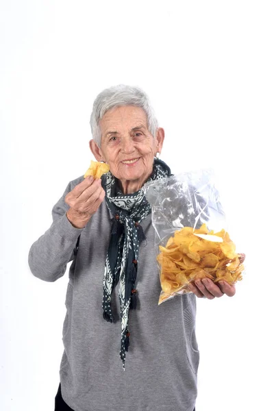 Senior kvinna äter chips på vit — Stockfoto