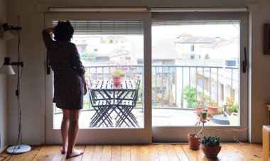 evde pencereden dışarı bakarak üzgün bir kadın