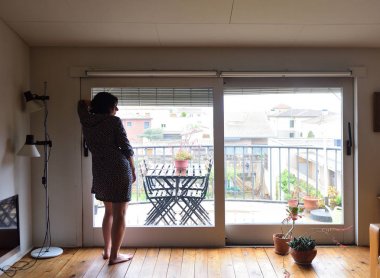 evde pencereden dışarı bakarak üzgün bir kadın