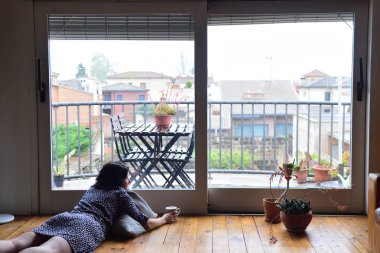 evde pencereden dışarı bakarak üzgün bir kadın