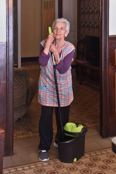 Oudere vrouw met mop maken van de verdieping van haar huis — Stockfoto