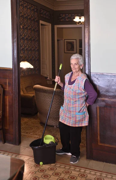 Oudere vrouw met mop maken van de verdieping van haar huis — Stockfoto
