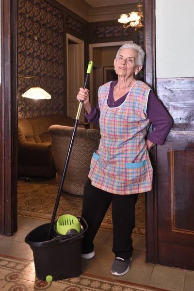 Oudere vrouw met mop maken van de verdieping van haar huis — Stockfoto