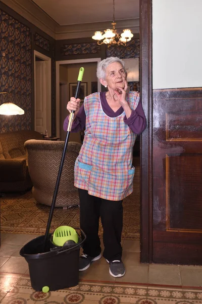 Oudere vrouw met mop maken van de verdieping van haar huis — Stockfoto