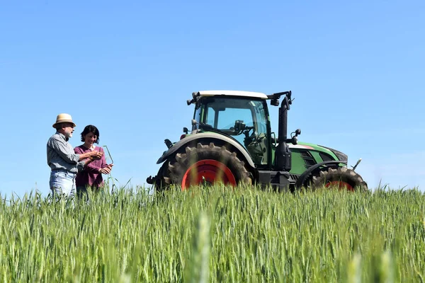 Coppia di contadini in un campo di grano con trattore — Foto Stock