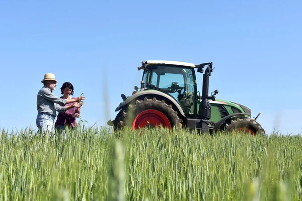 Coppia di contadini in un campo di grano con trattore — Foto Stock