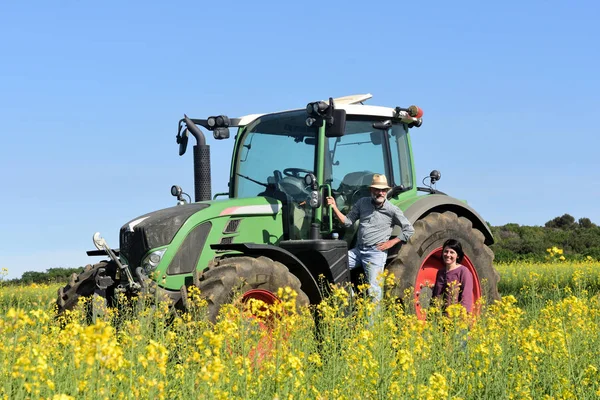 Casal de agricultores em um campo de canola com um trator — Fotografia de Stock