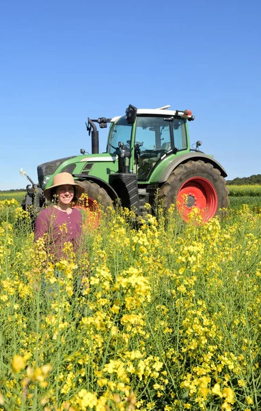 Donna contadina in un campo di colza con un trattore — Foto Stock
