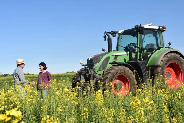 Casal de agricultores em um campo de canola com um trator — Fotografia de Stock