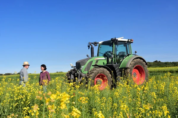 Casal de agricultores em um campo de canola com um trator — Fotografia de Stock