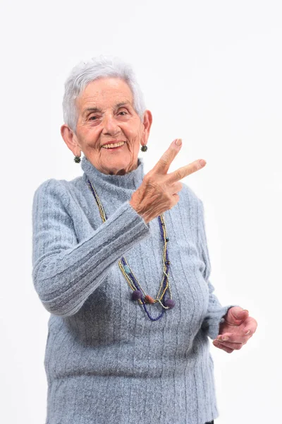 Femme plus âgée faisant le signe de la victoire sur un fond blanc — Photo