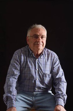 Siyah arka planda oturan kıdemli bir adamın portresi