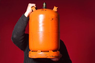 Kırmızı arka planda bir şişe bütan gazı tutan adam.