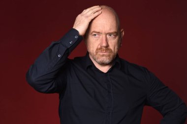 Kırmızı arka planda kafa üstü dalgın bir adam.