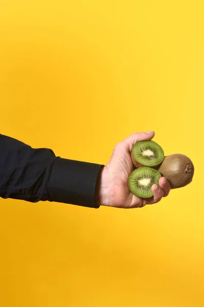 hand holding a group of kiwis on yellow background