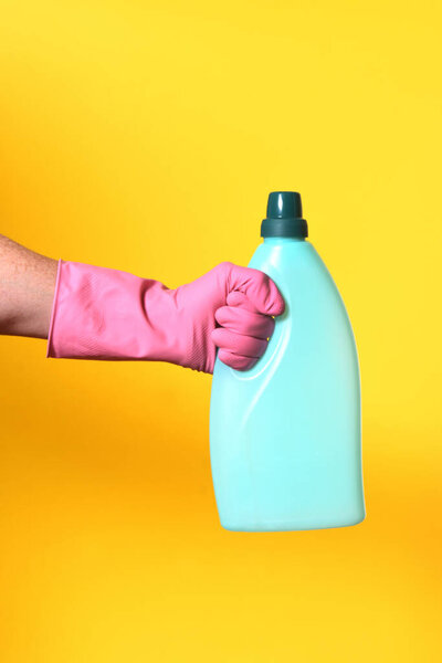 hand with glove and plastic bottle soap on yellow background