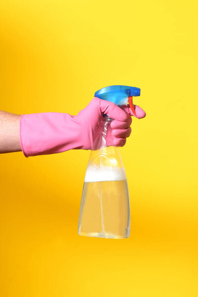 hand with spray bottle on yellow background